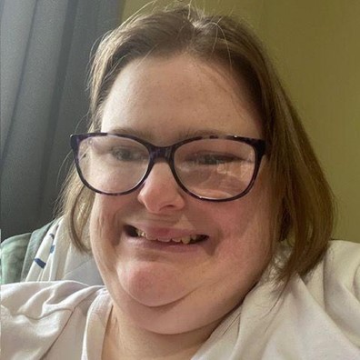 Jesse, a white female with shoulder length, light brown hair and glasses. She is smiling and wearing a white shirt.