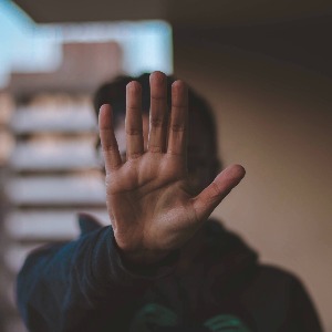 An individual facing the camera with their hand up, blocking view of their face, and indicating stop.