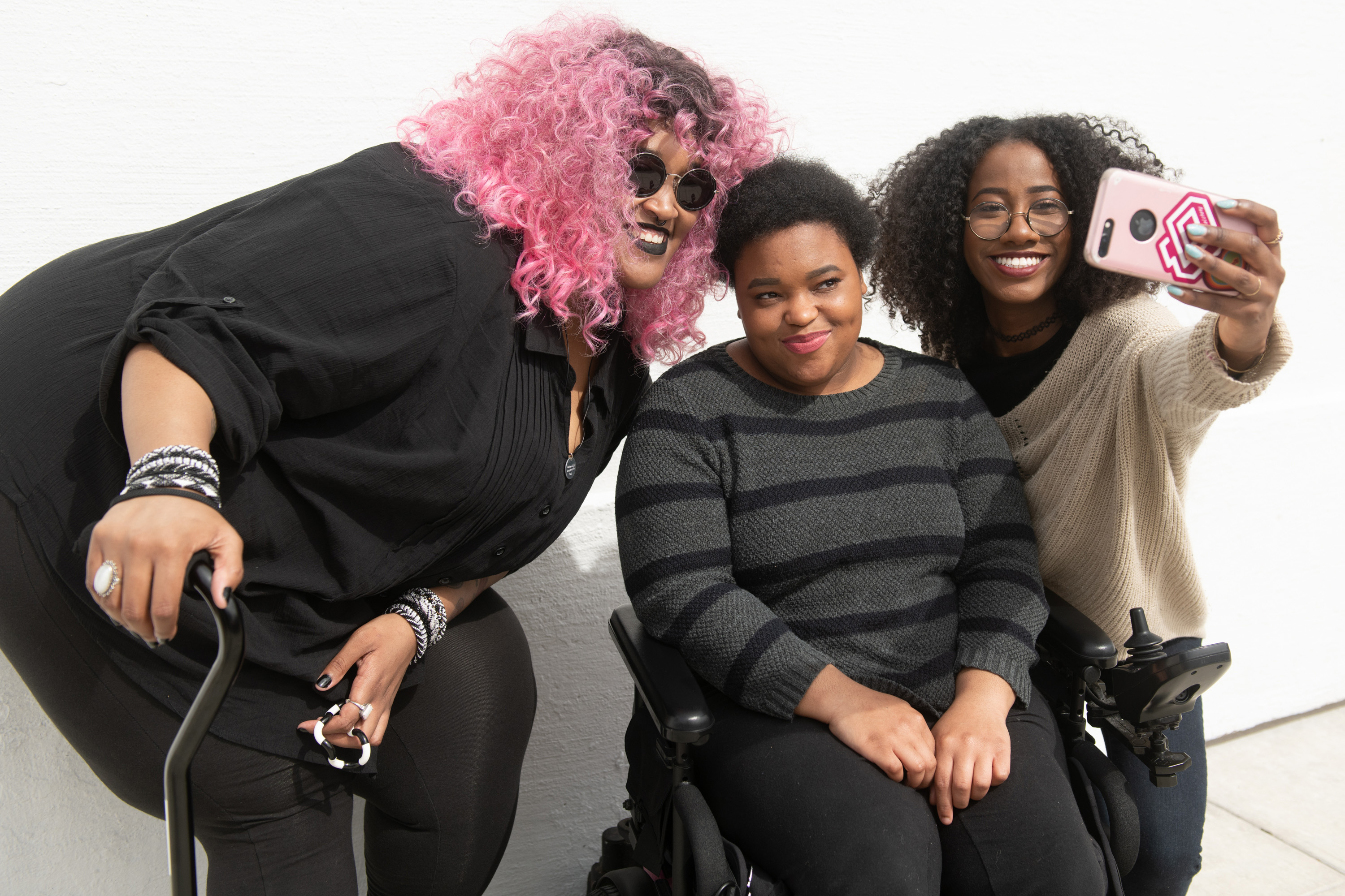 Three Black people of diverse genders and disabilities pose for a photo.