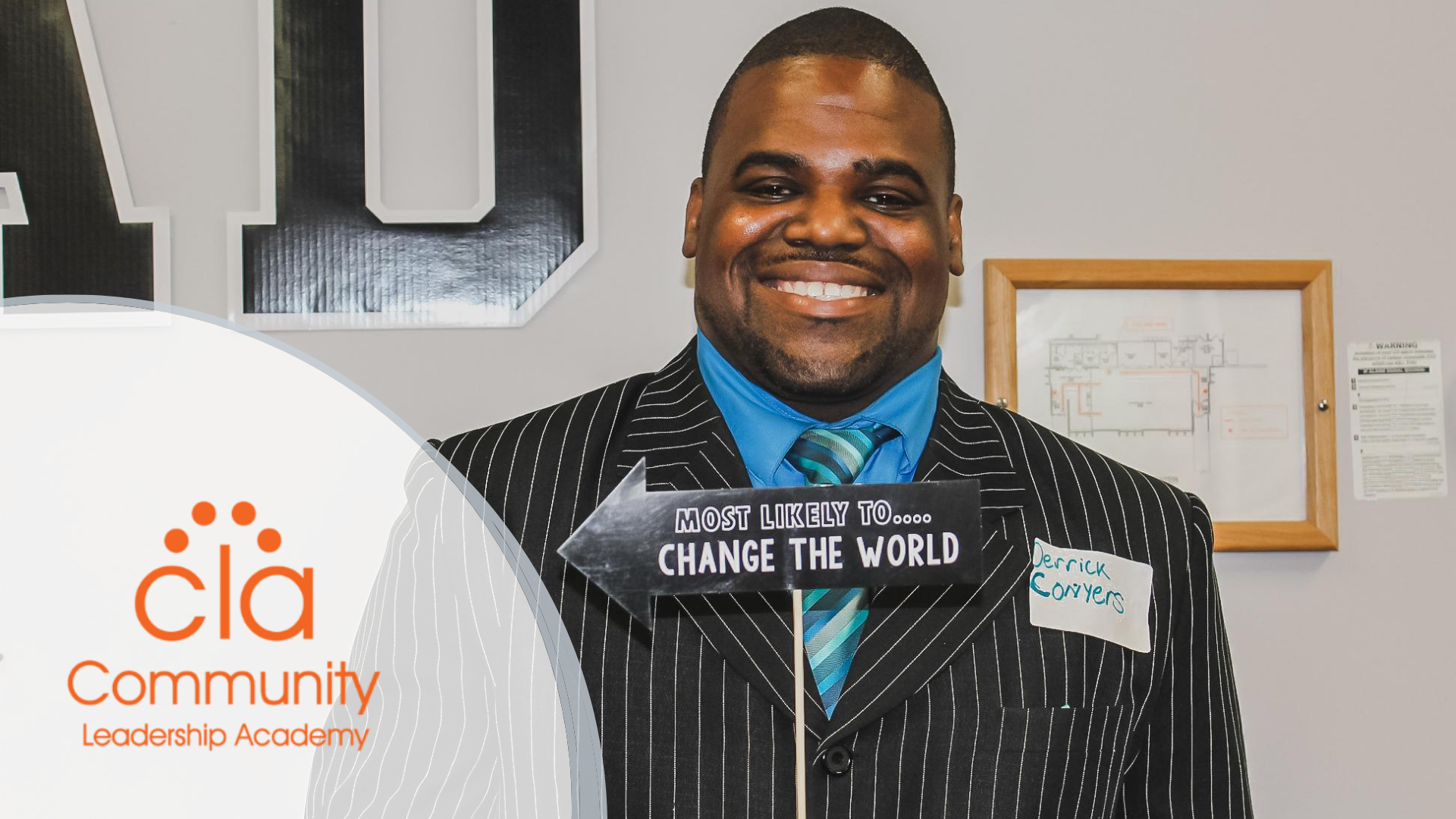 Photo of a Black man wearing a suit and tie, holding a sign that reads, 'Most likely to change the world,' while smiling. Community Leadership Academy Logo in orange appears in the left corner over a transparent white background