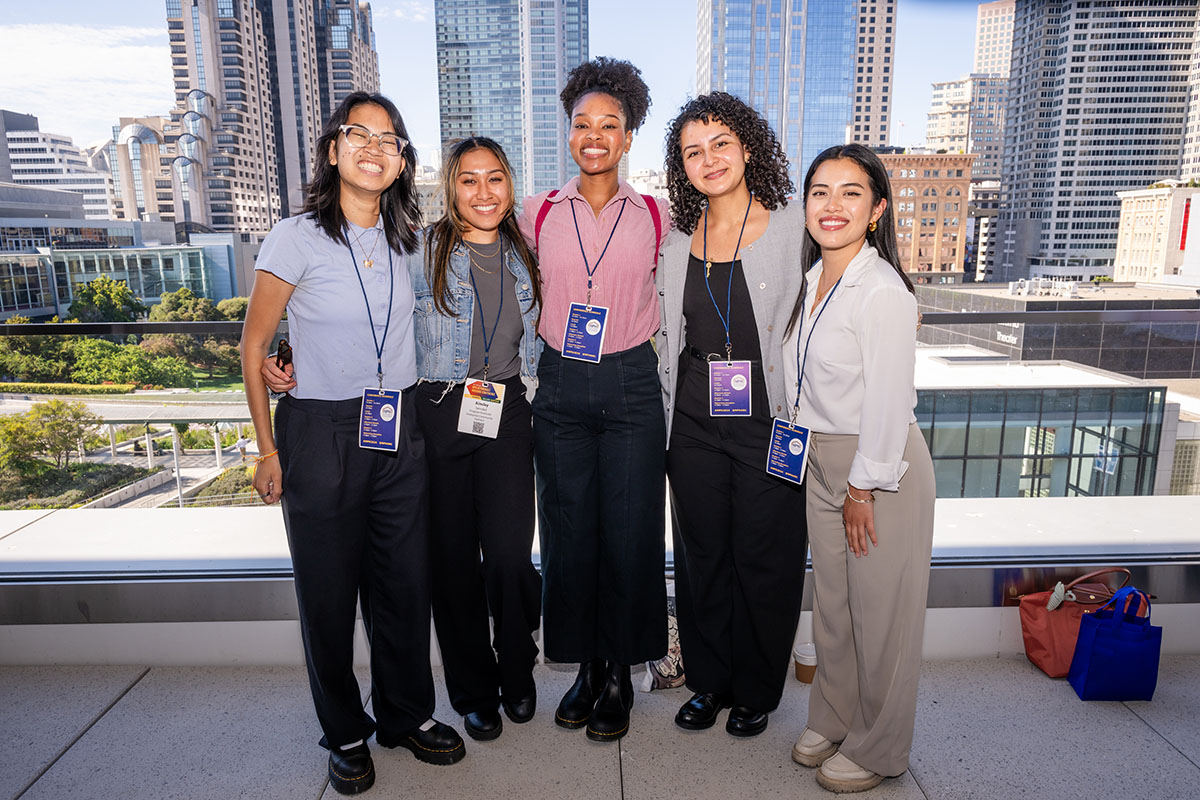 5 attendees posing on balcony with San Francisco in the background
