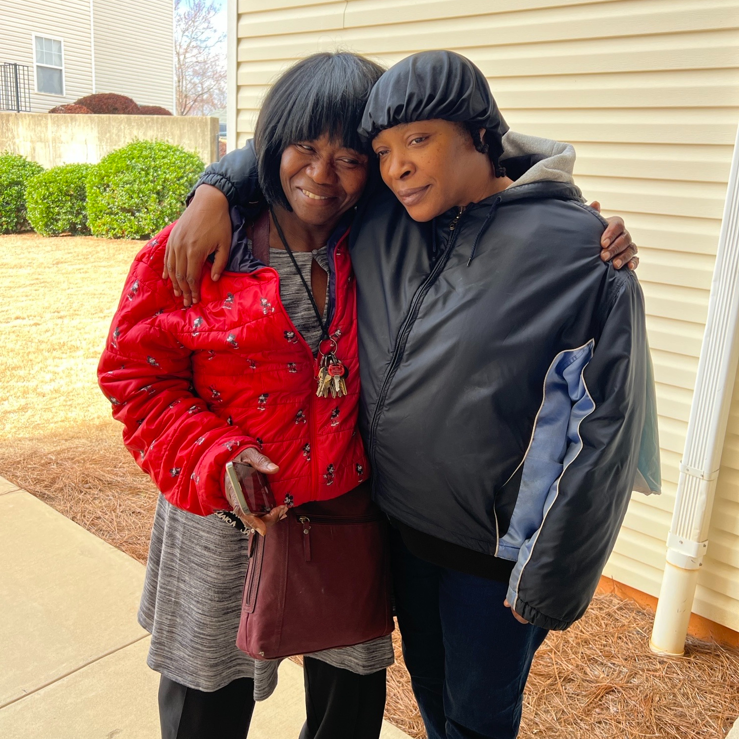Black woman with her family member, embracing outside her new home.