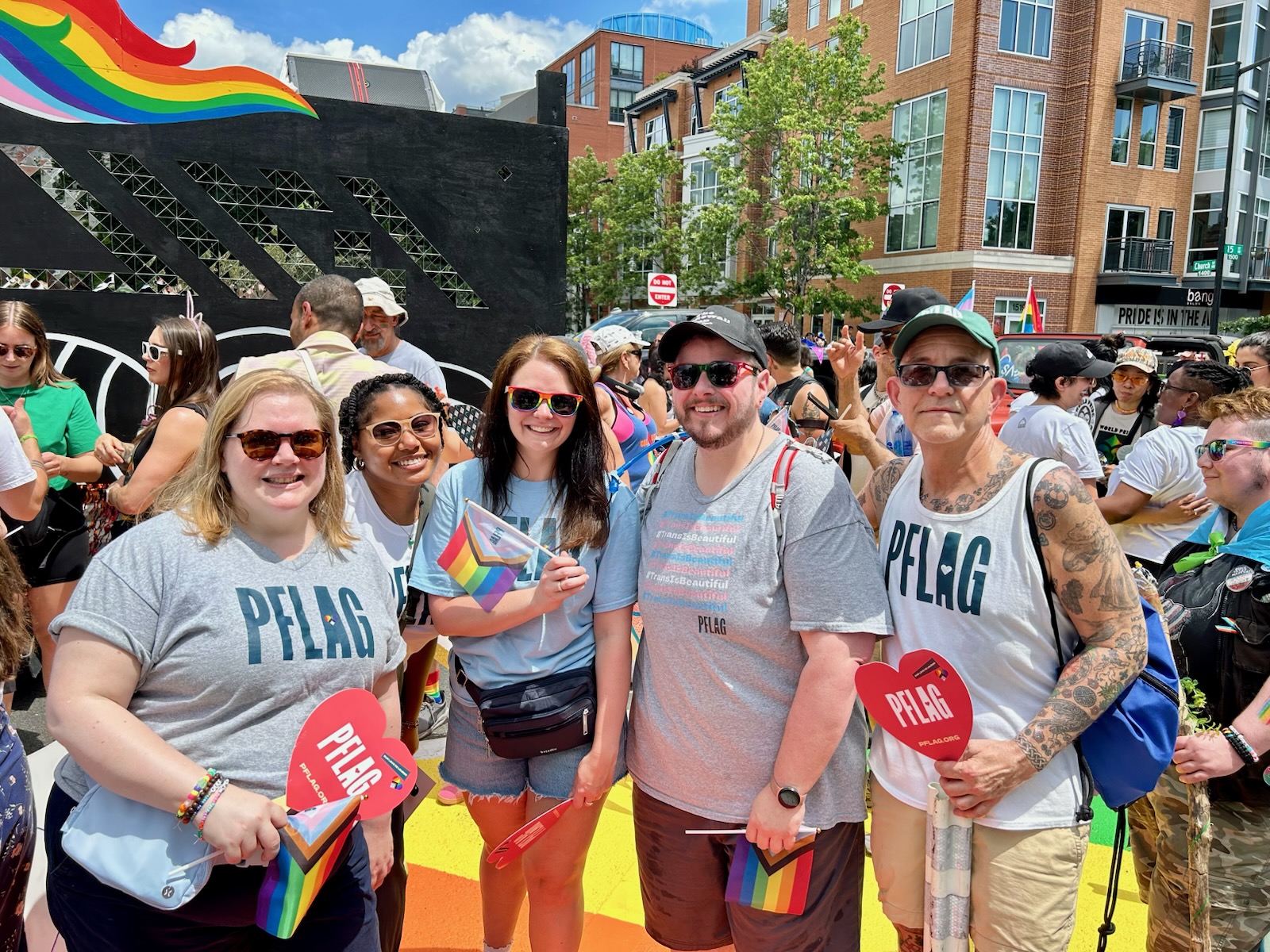 Image of staff of PFLAG at World Pride, wearing PFLAG logo t-shirts, carrying PFLAG logo fans, surrounded by people and rainbows.