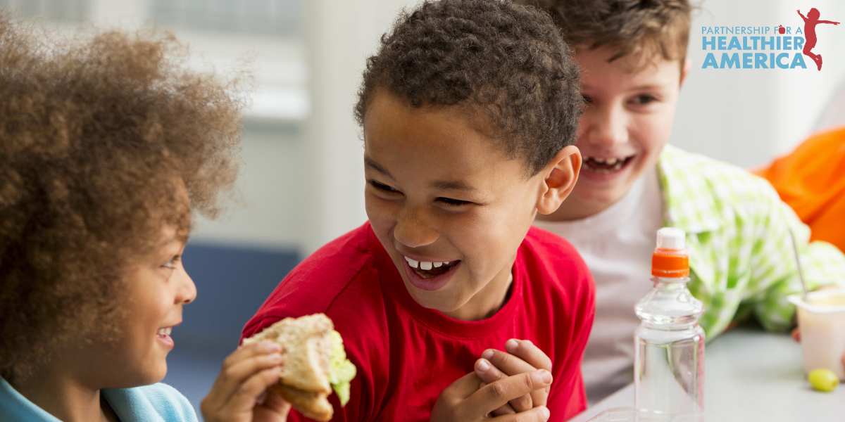 Children at lunch laughing - the blue and red PHA logo is in the upper-right corner