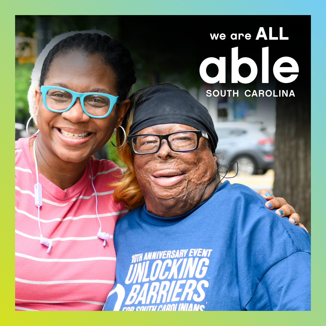 Able SC staffer Laquanda smiles with a friend at Advocacy day- both are Black women wearing glasses, Laquanda has visible burn scars and an advocacy day t-shirt. New slogan, 'we are all Able SC' is featured over the standard logo.