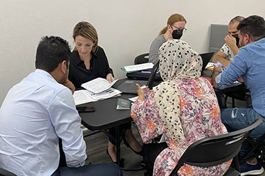 An Afghan woman with a headscarf sits at a table with an interpreter and a lawyer who is organizing paperwork.