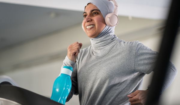 A smiling woman works out on a treadmill while wearing headphones