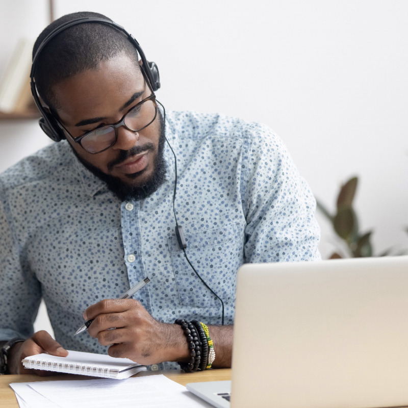 African American man seated in front of a laptop wearing headphones.