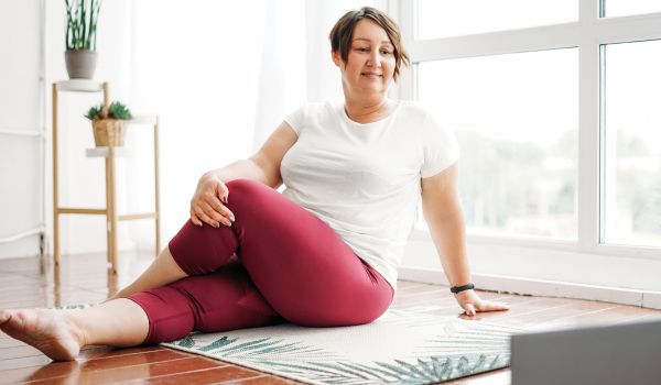 Photo of a middle-aged woman doing light stretches in her living room in front of a laptop