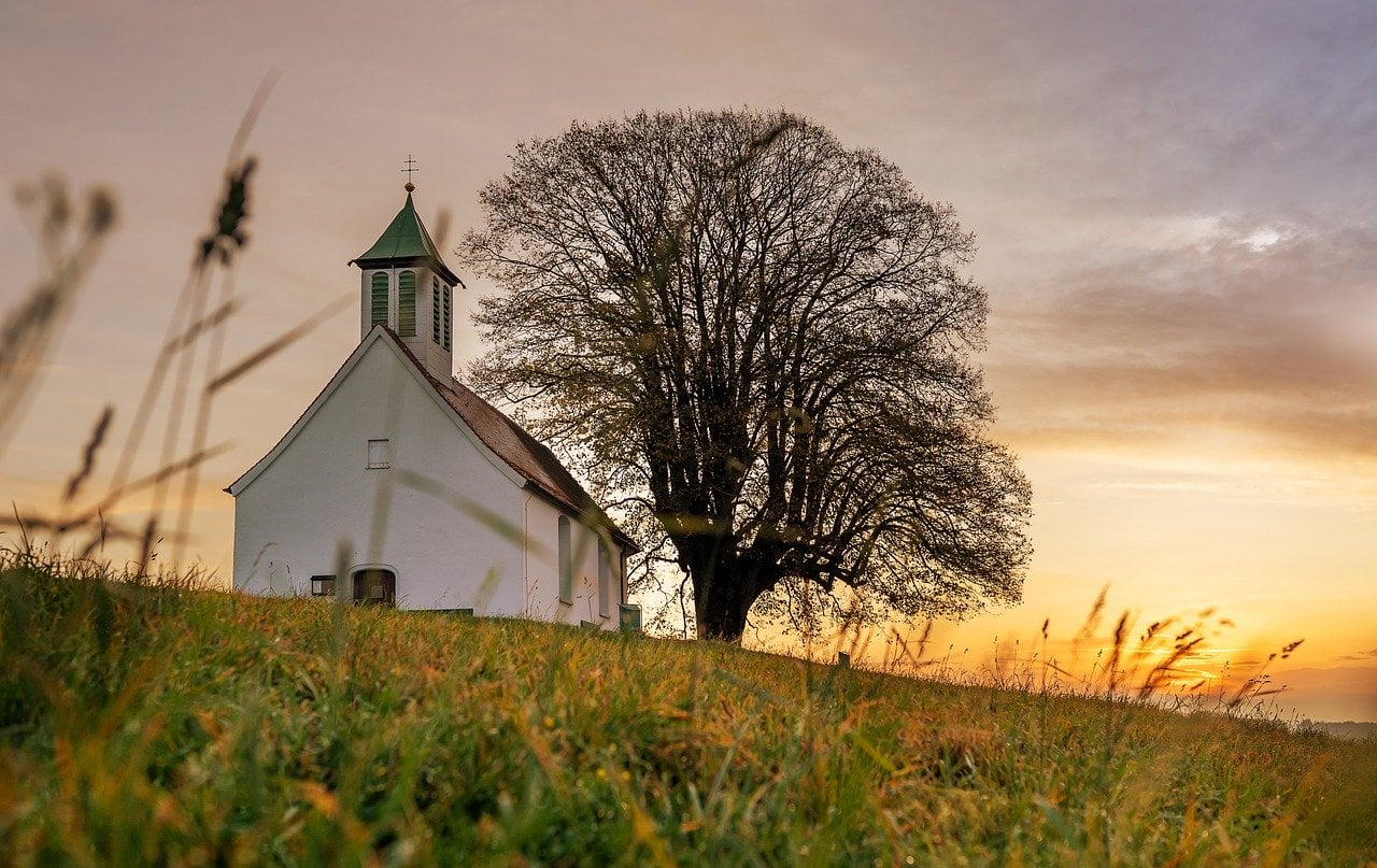 Church on the side of a hill, with the sun peaking behind the horizon.