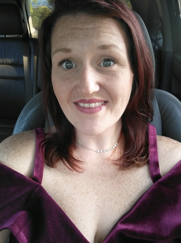 A white woman with brown hair wearing a purple top smiles at the camera