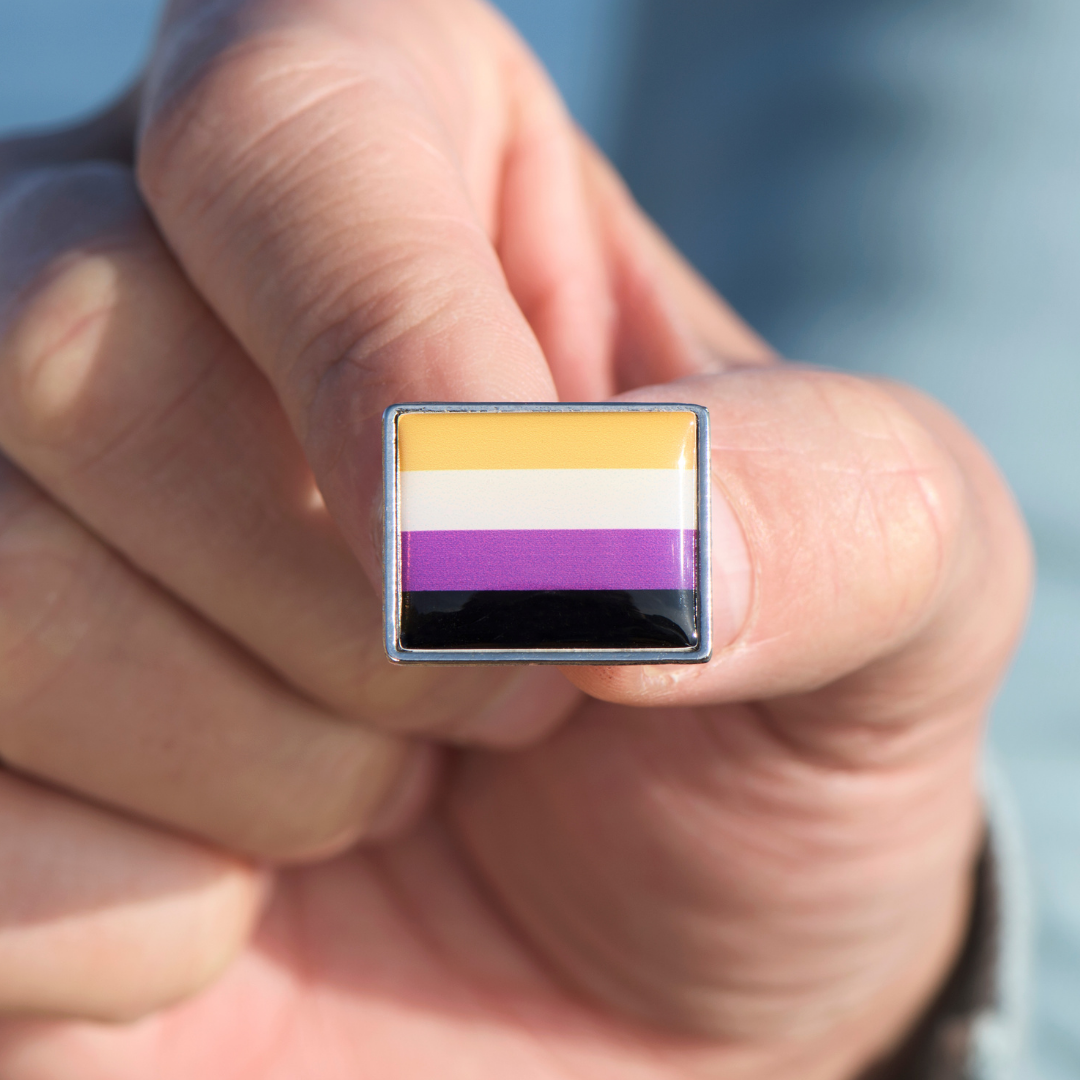 Hand holding a pin in the colors of the nonbinary Pride flag