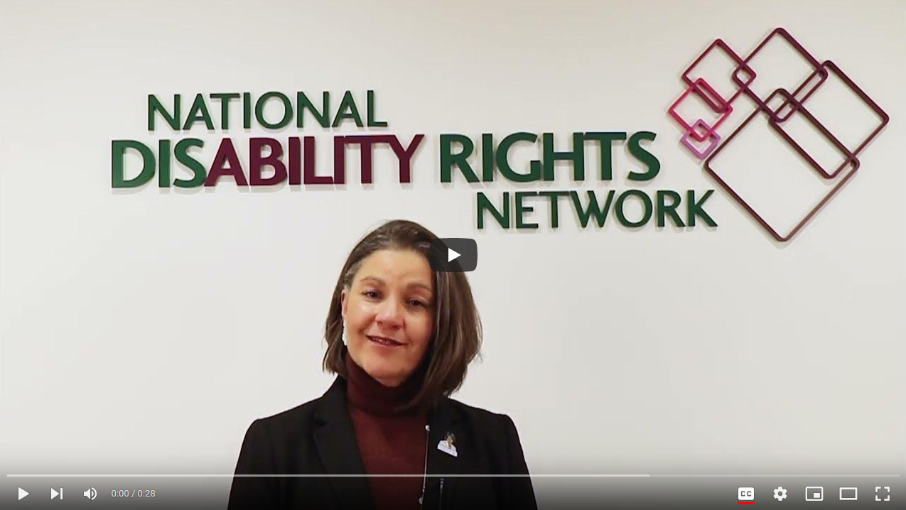 Still shot of a YouTube video. NDRN Executive Director Marlene Sallo is standing in front of a white wall with NDRN's logo above her.