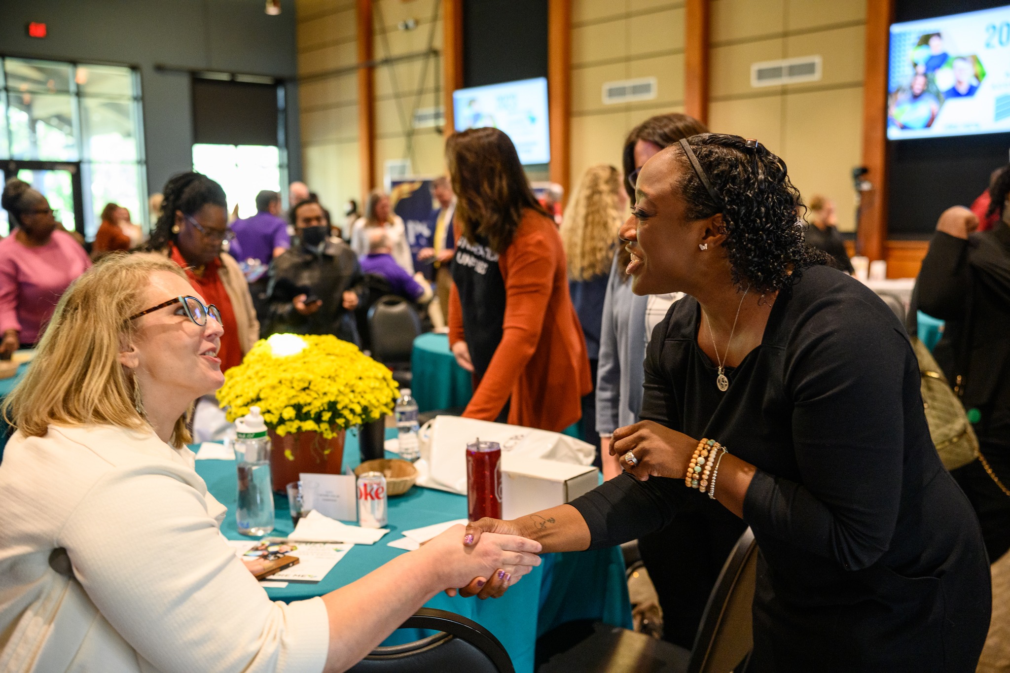 Able SC CEO, Kimberly Tissot, shaking hands with Dr. Sharp. Kimberly is a white woman with short blonde hair and glasses using crutches. Dr. Sharp is a black woman with short curly hair.